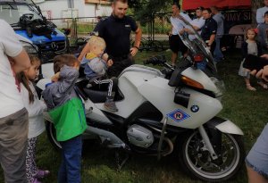 policjant przy motocyklu na nim dziecko obok inni ludzie