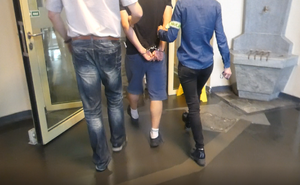 Dwaj policjanci nieumundurowani prowadzą zatrzymanego na czynności.