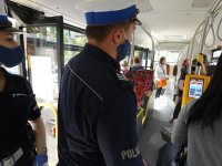 Policjanci umundurowani prowadzą kontrolę w środkach komunikacji zbiorowej w związku z obowiązkiem zasłaniania ust i nosa