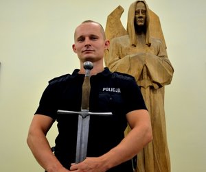 sierż. Kistela stoi trzymając miecz w rękach, obok rzeźba Michała Archanioła