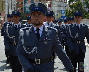 Policjanci z pocztu sztandarowego maszerują ulicami miasta. Na zdjęciach widać policjantów idących w szeregach