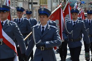 Policjanci z pocztu sztandarowego maszerują ulicami miasta. Na zdjęciach widać policjantów idących w szeregach