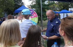 na pikniku. Dzieci i dorośli oglądają stoiska policyjne, na nich policjanci pokazują materiały profilaktyczne, konkursy, prezentują swoje pasje