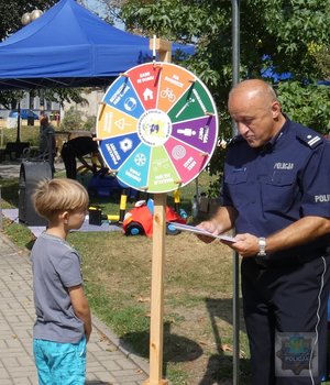 na pikniku policyjnym: dzieci biorą udział w kole fortuny - konkursie z nagrodami - policjant-rycerz pokazuje zbroje, policjant-malarz pokazuje swoje obrazy, komandosi policyjni prezentują uzbrojenie